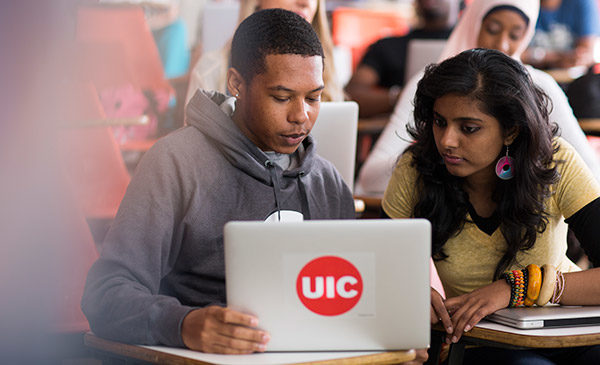 students looking at a laptop with the U I C logo
